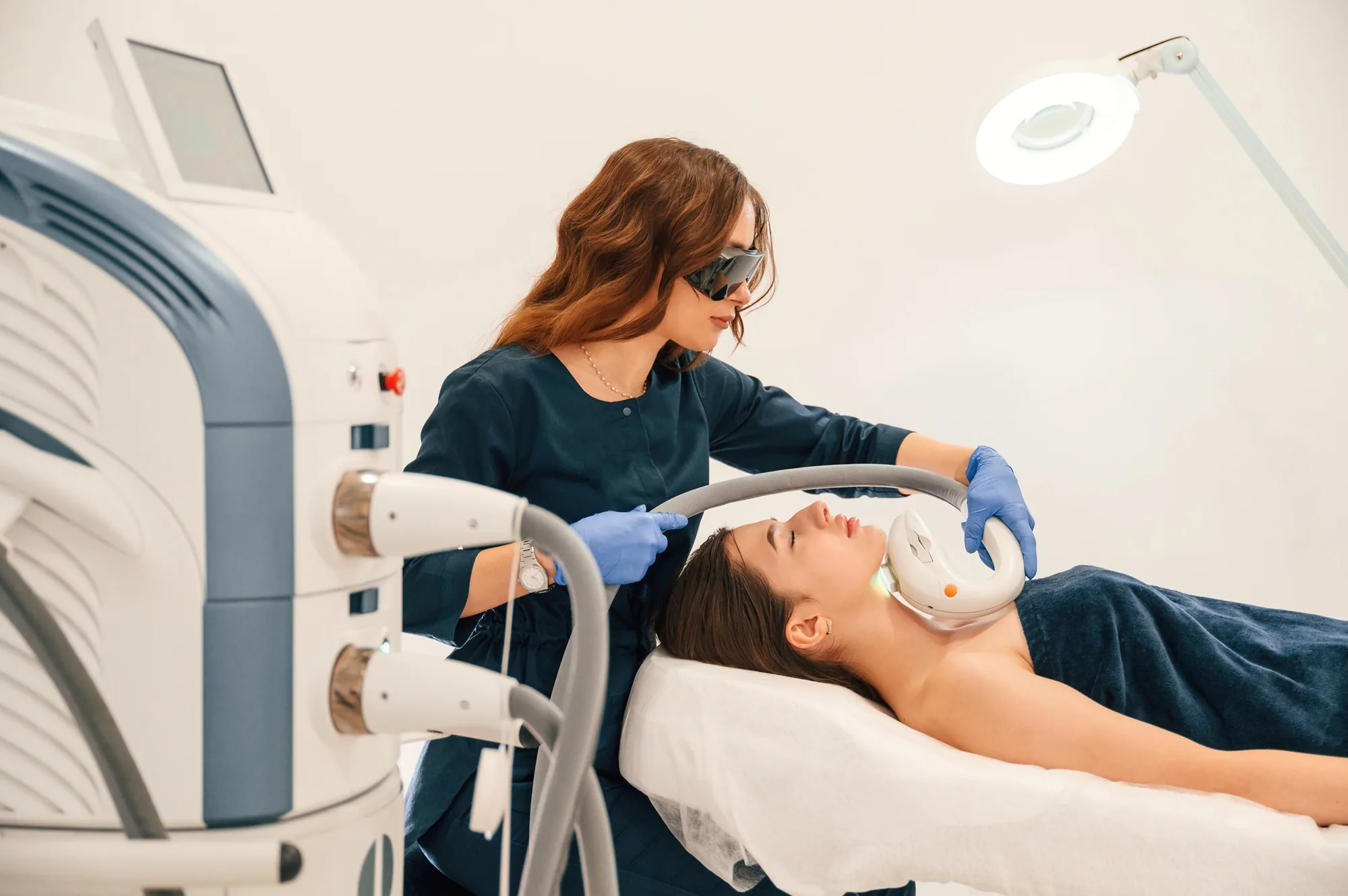 Cosmetologist performing a laser neck treatment on a woman resting on a treatment table